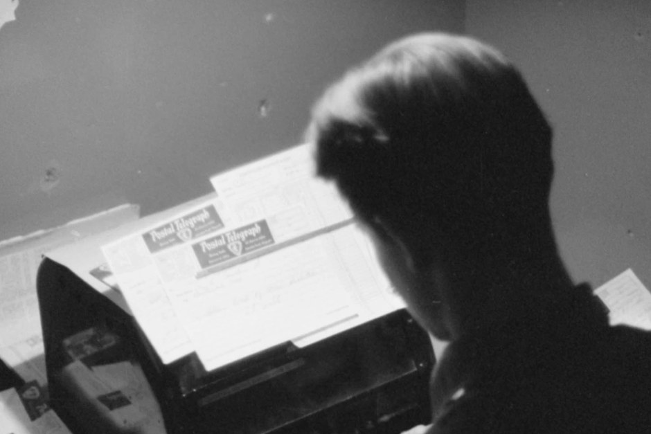 A person working at a typewriter in a quiet monochrome scene.
